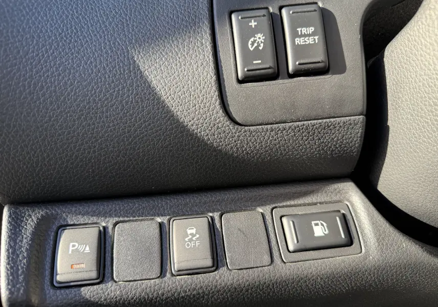 Gros plan sur les boutons de commande noirs du tableau de bord du Renault Alaskan brun 2018, avec réglage éclairage et contrôle traction.