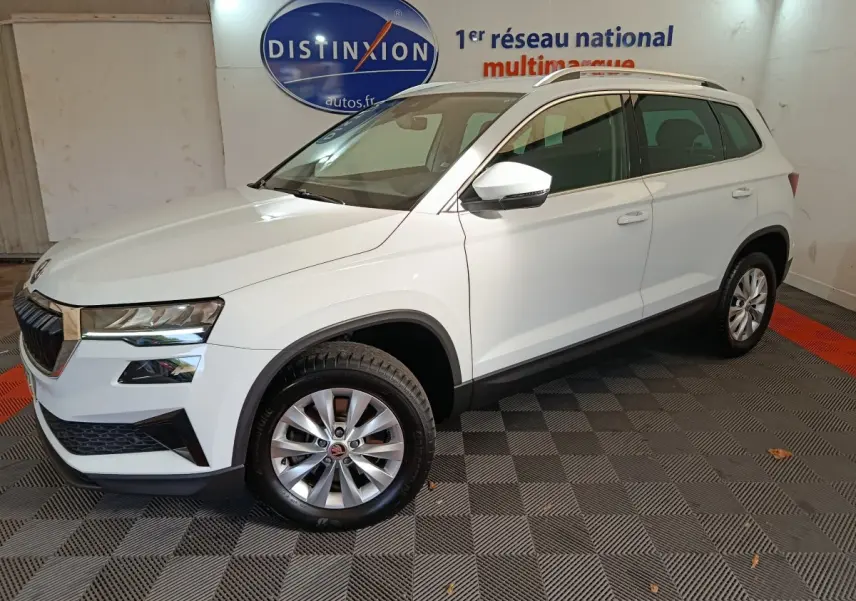 Vue 3/4 avant droit d'un Skoda Karoq blanc 2024 avec jantes alliage et rétroviseurs blancs dans un showroom.