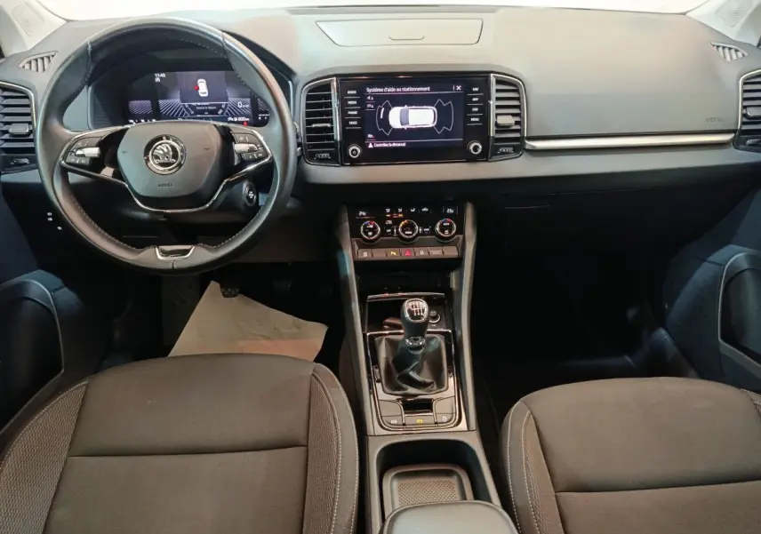 Vue intérieure avant du Skoda Karoq 2024 avec tableau de bord noir, volant cuir multifonctions et écran tactile central.
