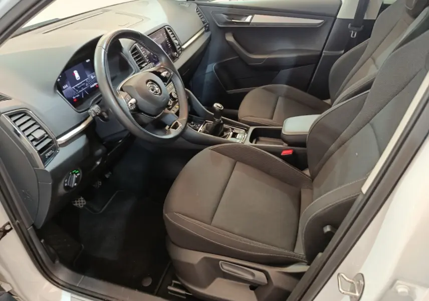 Vue intérieure côté conducteur du Skoda Karoq blanc 2024, montrant sièges noirs, volant cuir et tableau de bord digital.