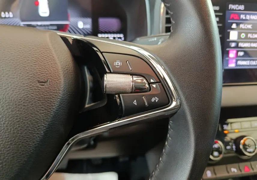 Gros plan sur les commandes multifonctions côté gauche du volant cuir du Skoda Karoq 2024, intérieur noir.