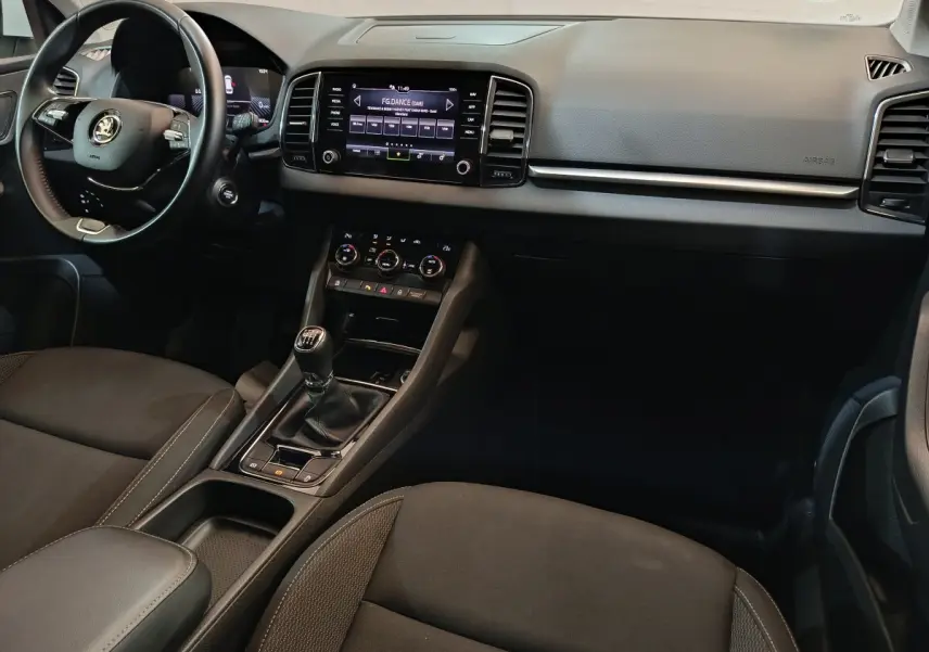 Vue intérieure avant du Skoda Karoq 2.0 TDI 2024, tableau de bord noir avec écran tactile et volant cuir multifonctions.