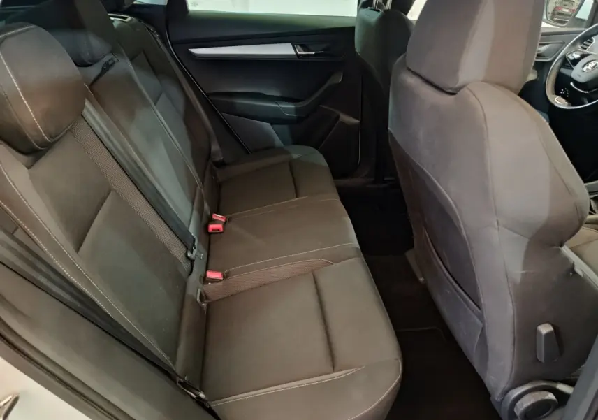 Vue intérieure arrière côté gauche du Skoda Karoq 2024 blanc, sièges tissu gris foncé avec ceintures visibles.