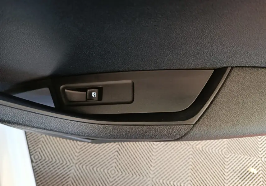 Gros plan sur le bouton de commande de la vitre électrique côté porte intérieure d'une Skoda Karoq blanche.