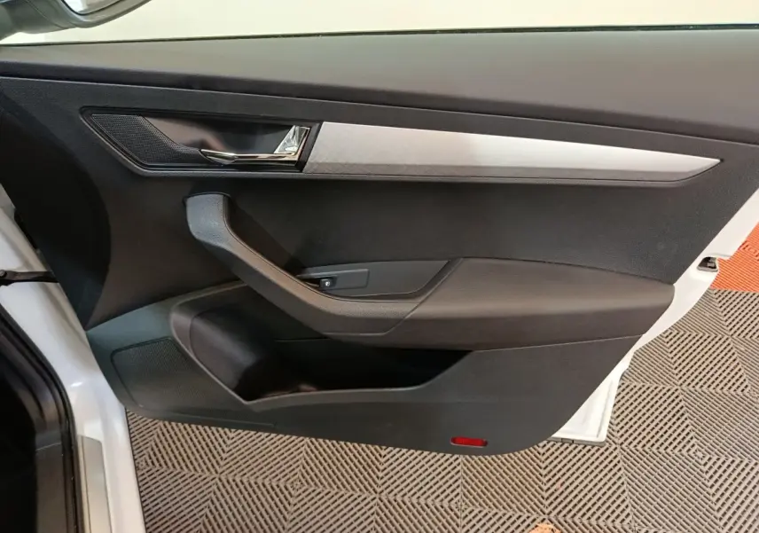 Intérieur côté gauche de la porte avant d’un Skoda Karoq blanc, avec poignée noire et insert décoratif argenté.