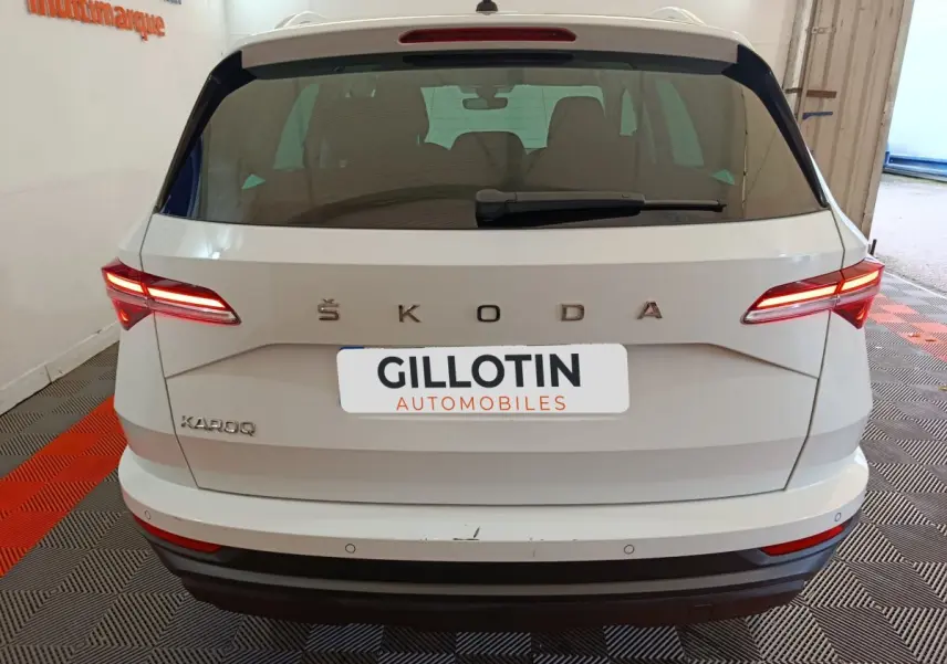 Vue arrière d'un Skoda Karoq blanc 2024 avec feux LED allumés et logo ŠKODA visible sur un sol à damier.