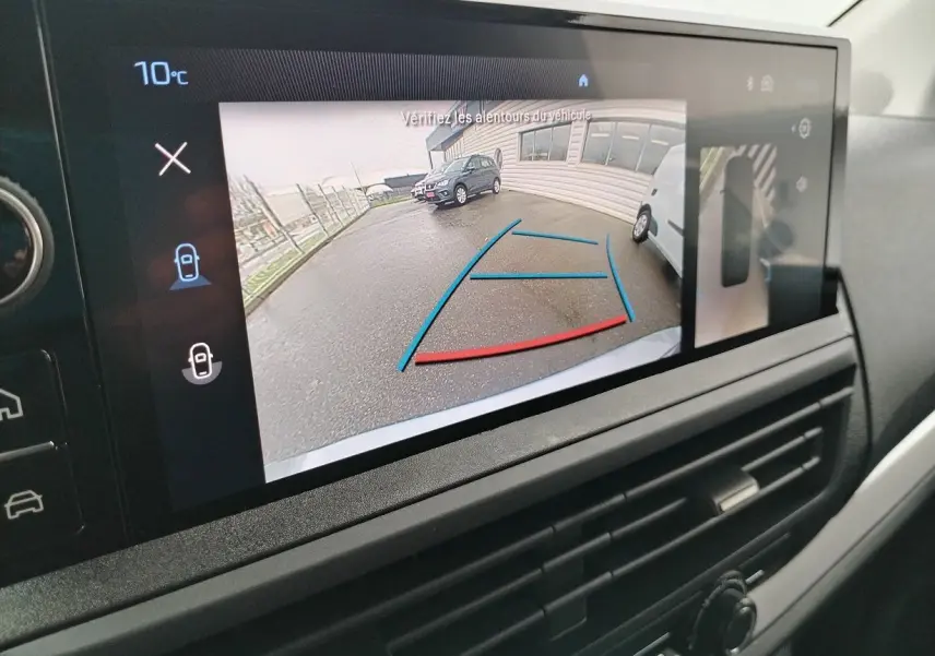 Écran multimédia montrant la caméra de recul avec vue arrière sur un parking sous temps gris.