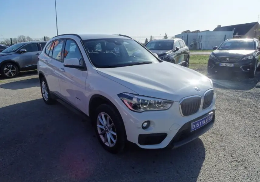 BMW X1 sDrive 18d blanc vue 3/4 avant droit, avec calandre caractéristique et feux LED allumés.
