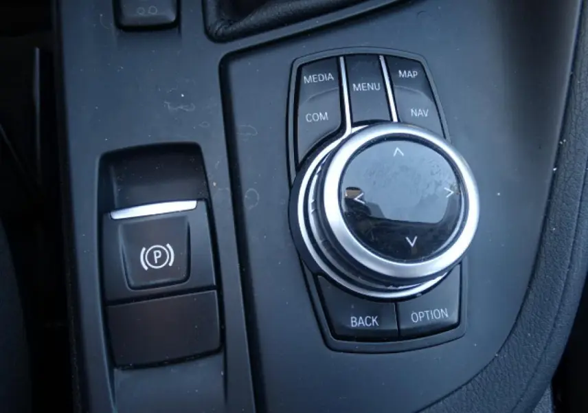 Gros plan sur la molette de commande iDrive et le frein à main électronique dans le BMW X1 sDrive 18d blanc.