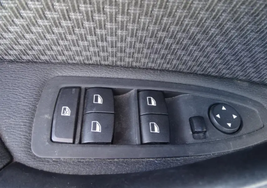 Gros plan sur les commandes de lève-vitres et rétroviseurs côté conducteur d'une BMW X1 blanche de 2017.