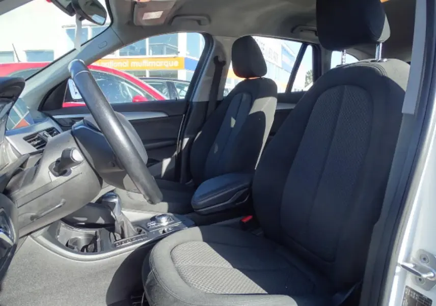 Vue intérieure côté conducteur du BMW X1 blanc 2017, sièges tissu noirs et volant multifonction cuir.