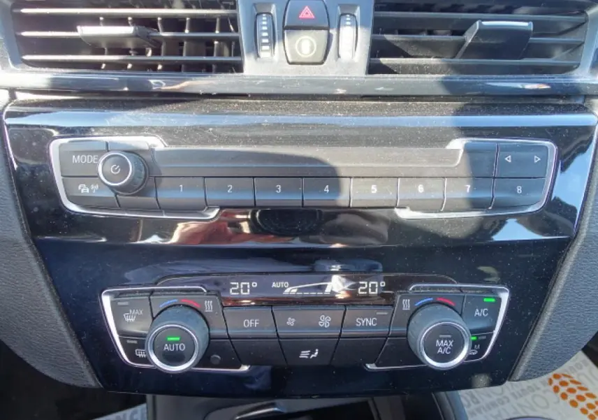 Vue rapprochée de la console centrale noire du BMW X1 blanc, montrant les commandes de climatisation automatique 2 zones.