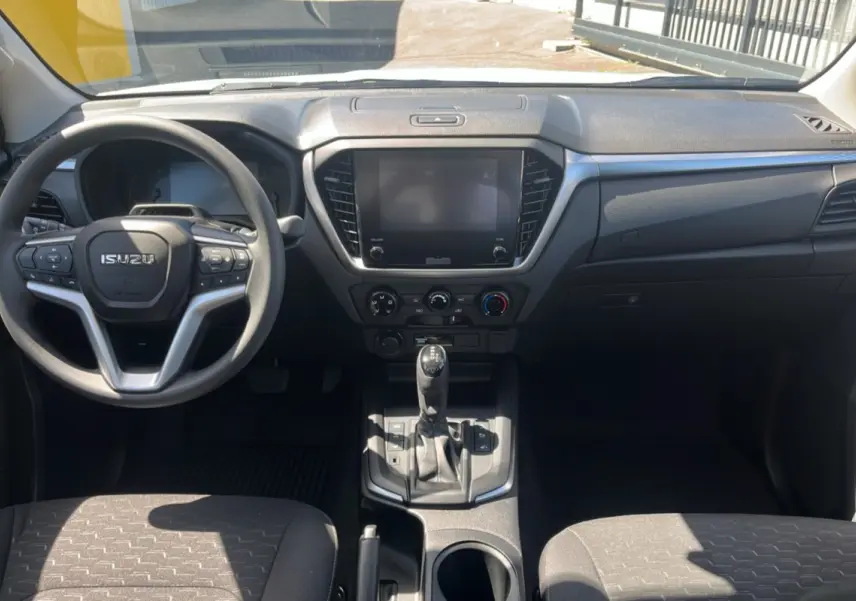 Vue intérieure avant de l'Isuzu D-MAX 2026 avec tableau de bord noir, volant multifonctions et écran tactile central éteint.
