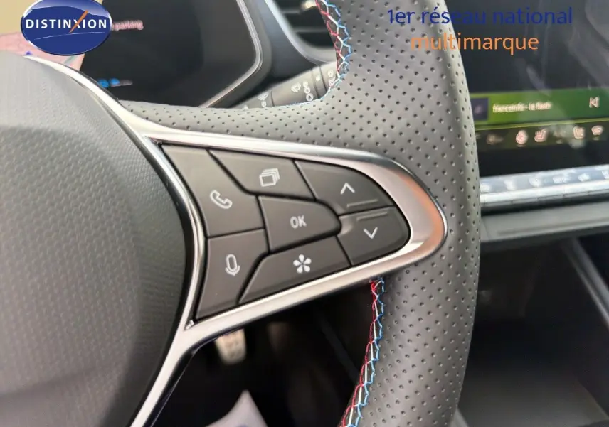 Gros plan sur le volant perforé avec surpiqûres tricolores de la Renault Symbioz gris cassiopée, affichage digital en arrière-plan.