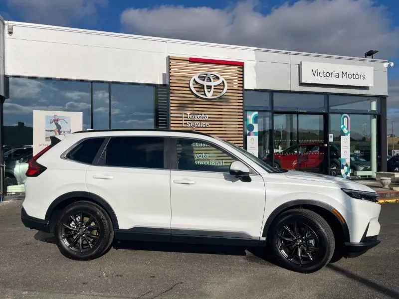 Vue de profil côté gauche d'un Honda CR-V 2024 blanc Diamant Brillant Premium avec jantes noires devant un concessionnaire Toyota.