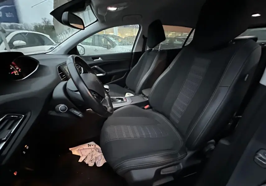 Vue intérieure côté conducteur de la Peugeot 308 gris Artense, montrant sièges avant en tissu et tableau de bord moderne.