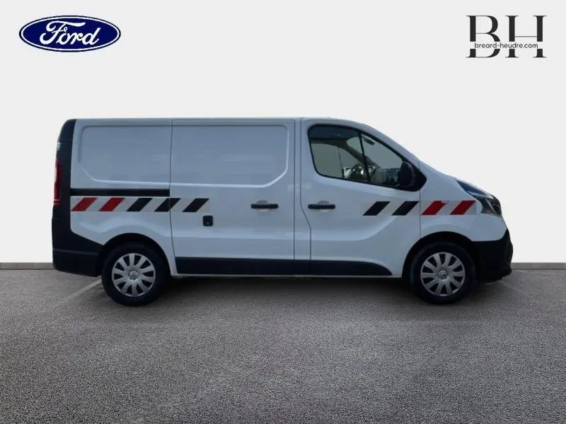 Fourgon Renault Trafic blanc glacier vu de profil côté gauche avec bandes rouges et noires sur la carrosserie.