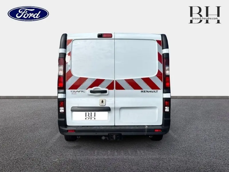 Vue arrière d'un Renault Trafic Fourgon blanc Glacier avec marquages rouges en diagonale et attelage de remorque visible.