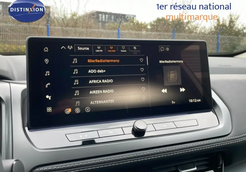 Vue intérieure centrée sur l'écran tactile multimédia du Nissan Qashqai blanc nacré 2025, affichant les stations radio.