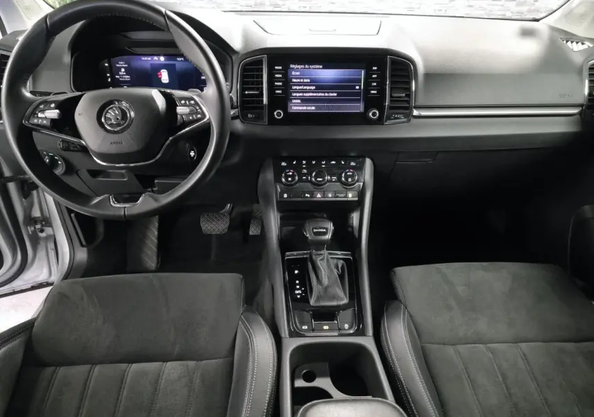 Vue intérieure avant du Skoda Karoq 2023 gris, montrant tableau de bord, volant cuir multifonctions et console centrale avec écran tactile.