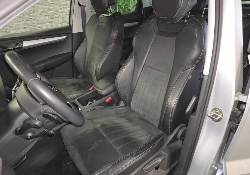 Vue intérieure côté conducteur du Skoda Karoq 2023, sièges en cuir noir avec surpiqûres blanches et volant multifonction.