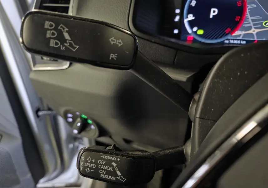 Gros plan sur les commandes au volant du Skoda Karoq 2023, avec affichage numérique et portière grise ouverte en arrière-plan.