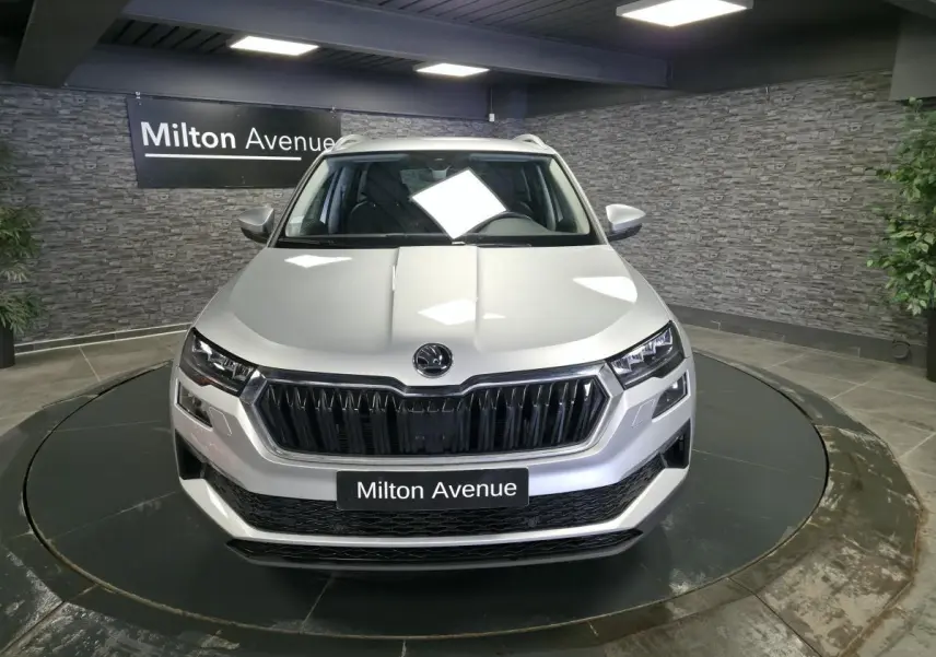 Vue avant d’un Skoda Karoq gris 2023 exposé en showroom avec calandre noire et phares LED distinctifs.