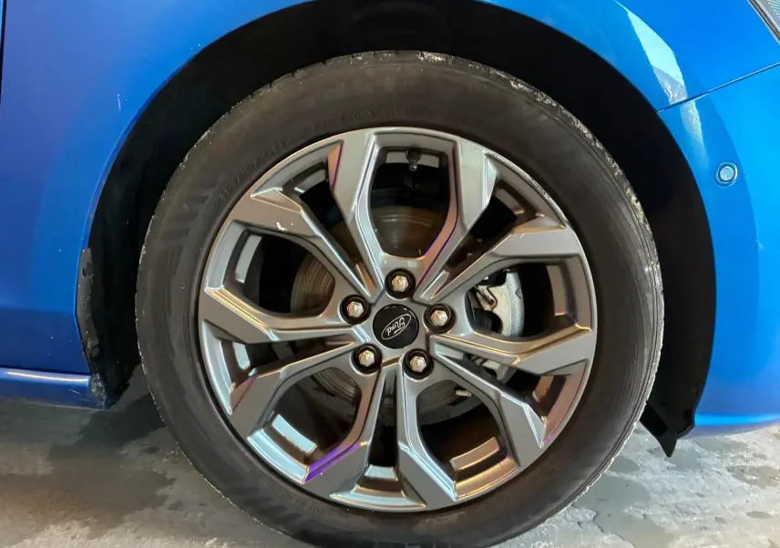 Gros plan sur la roue avant gauche d'une Ford Focus bleu 2024, mettant en valeur la jante alliage au design moderne.