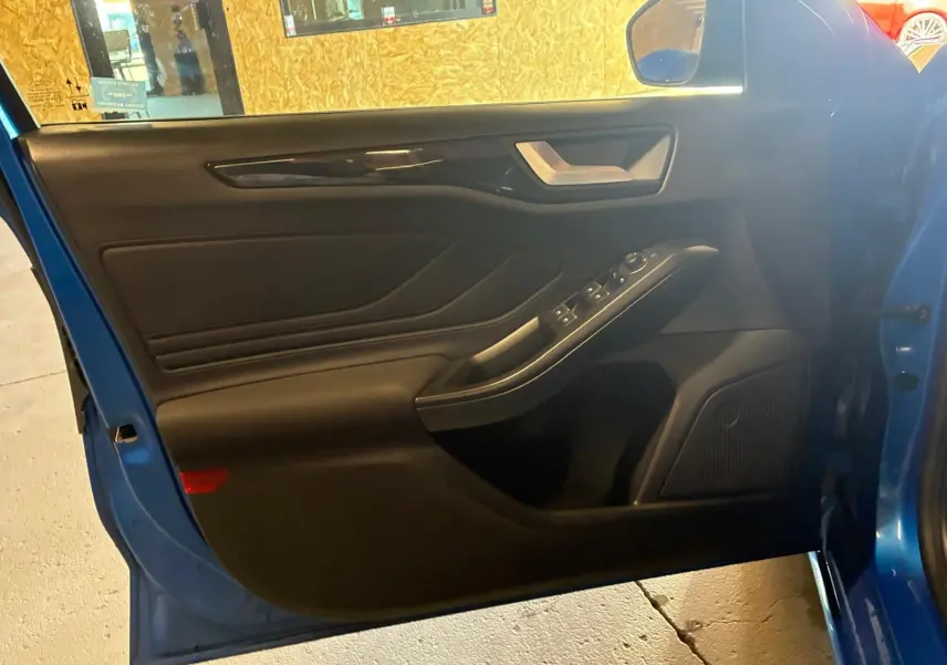 Vue intérieure de la porte avant gauche d’une Ford Focus bleu 2024, avec commandes électriques et garniture noire.