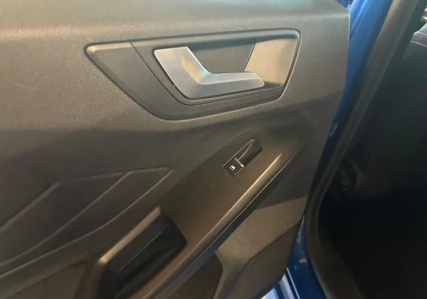 Détail de la porte intérieure côté gauche d'une Ford Focus bleu 2024, avec poignée argentée et bouton de vitre électrique.