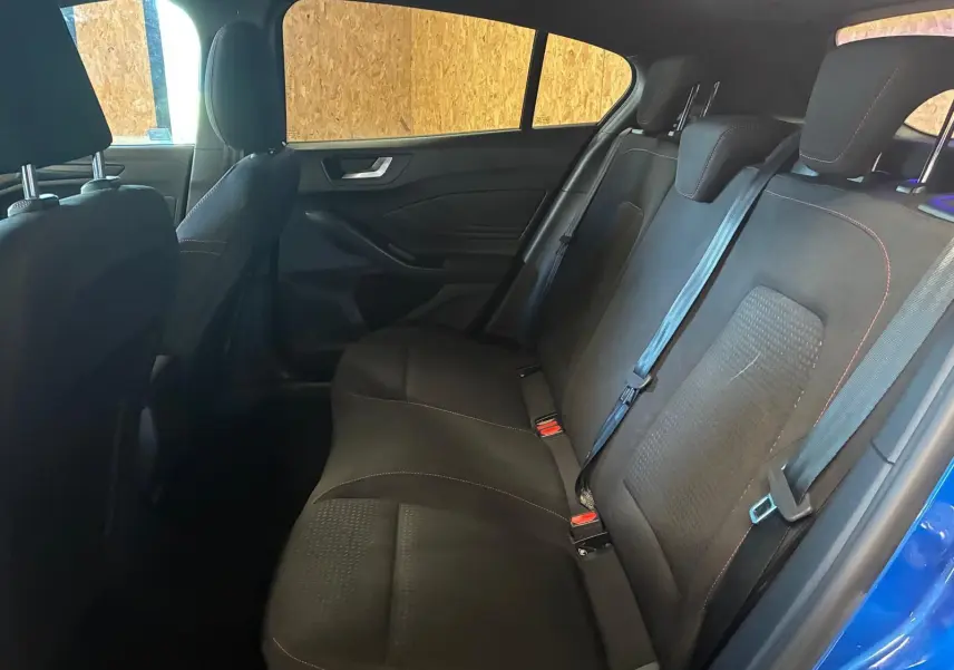 Vue intérieure côté droit des sièges arrière noirs en tissu avec surpiqûres rouges d'une Ford Focus 2024 bleue.