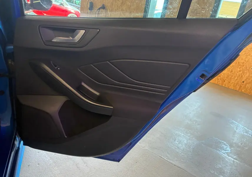 Vue rapprochée de la porte arrière gauche bleu vif d’une Ford Focus 2024, avec garniture intérieure noire et poignée argentée.