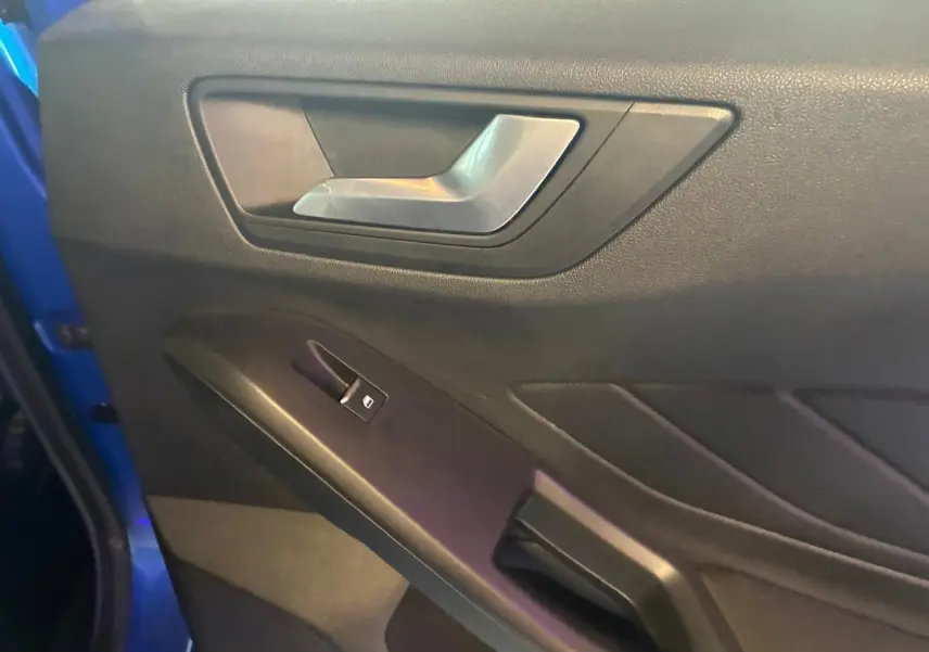 Gros plan sur la poignée intérieure et le bouton de lève-vitre côté gauche d’une Ford Focus bleu 2024.