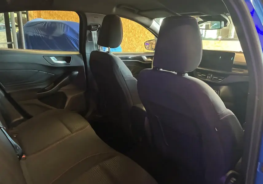 Vue intérieure arrière côté gauche de la Ford Focus 2024 bleu, sièges tissu noirs avec surpiqûres rouges et tableau de bord visible.
