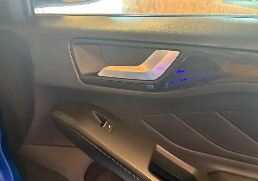 Détail de la porte intérieure côté gauche de la Ford Focus bleu 2024, avec poignée argentée et commande de fenêtre.