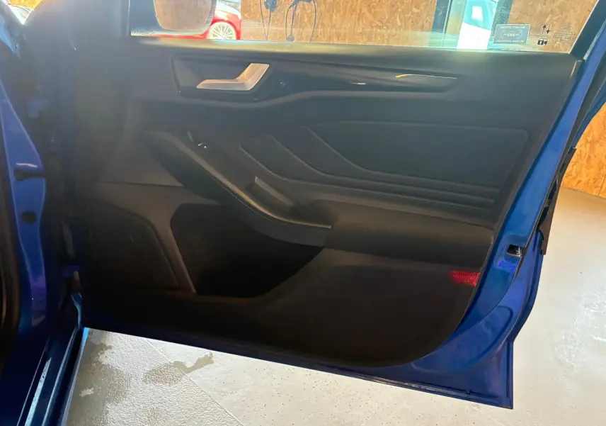 Vue intérieure de la porte avant gauche bleu vif d'une Ford Focus 2024, avec panneau noir et poignée argentée.