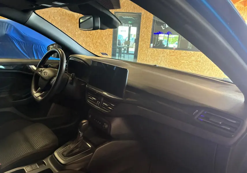 Vue intérieure côté conducteur de la Ford Focus 2024 bleu, montrant le tableau de bord et la console centrale avec écran tactile.