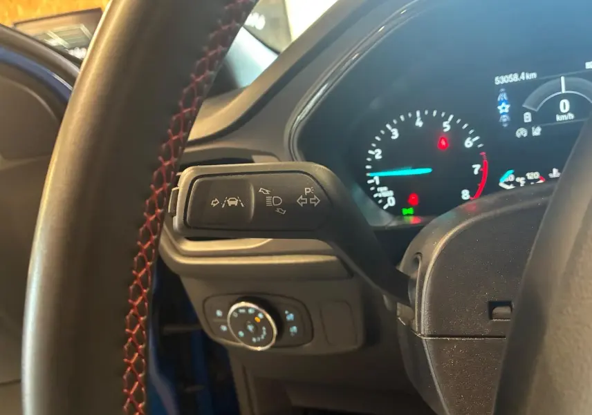 Vue rapprochée du commodo gauche et du tableau de bord numérique d’une Ford Focus bleue 2024, intérieur noir.