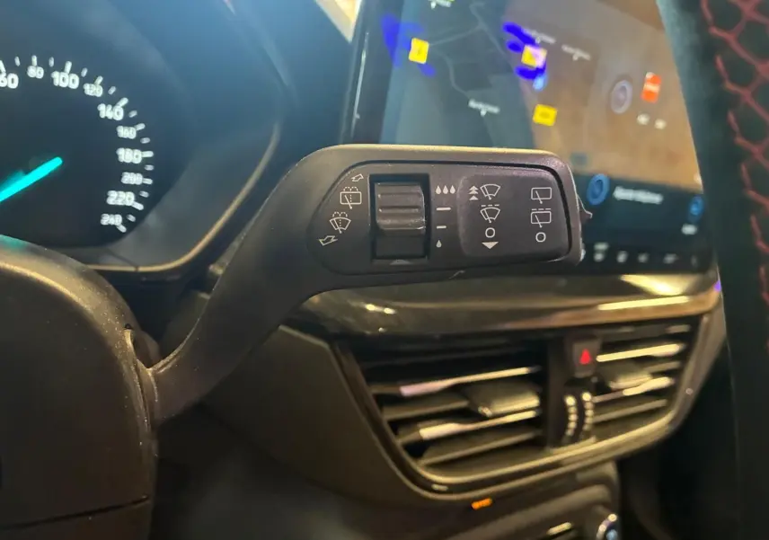 Gros plan sur la commande d’essuie-glace à gauche du volant dans l’habitacle noir de la Ford Focus bleu 2024.