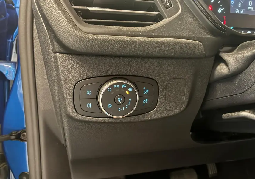 Gros plan sur le panneau de commande des phares à gauche du volant dans l’habitacle noir d’une Ford Focus bleue 2024.