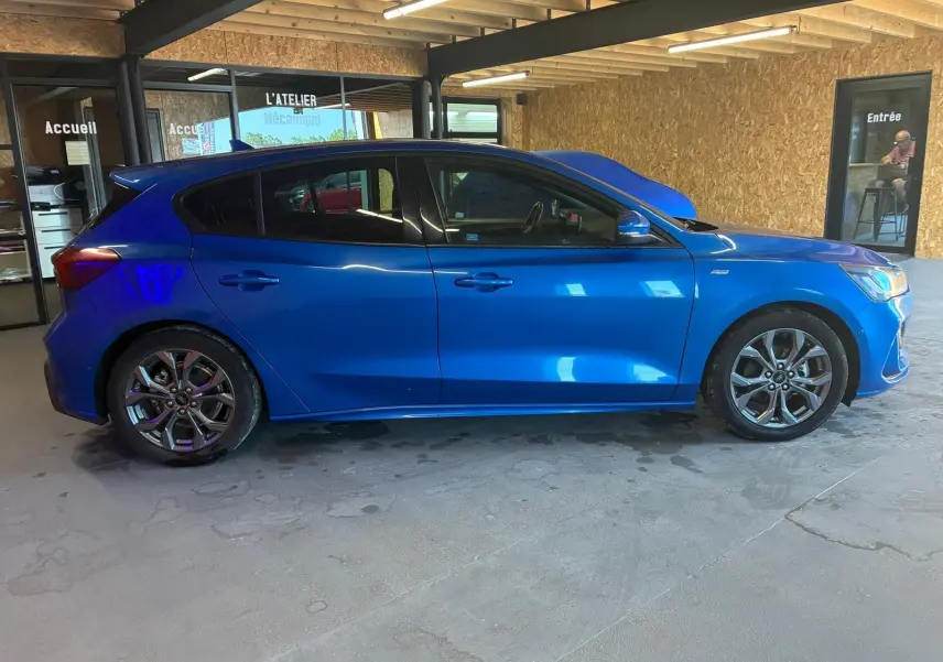Vue de profil côté gauche d'une Ford Focus 2024 bleu vif, finition ST Line avec jantes alliage et vitres teintées.