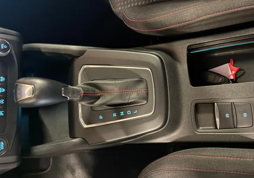 Vue rapprochée de la console centrale d’une Ford Focus bleue 2024, avec levier de vitesse automatique et coutures rouges sur les sièges.