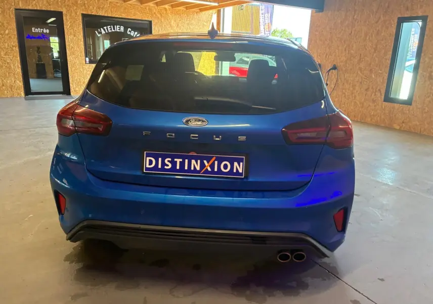 Vue arrière d'une Ford Focus bleu 2024 avec double sortie d'échappement et logo Distinxion visible en intérieur d'atelier.