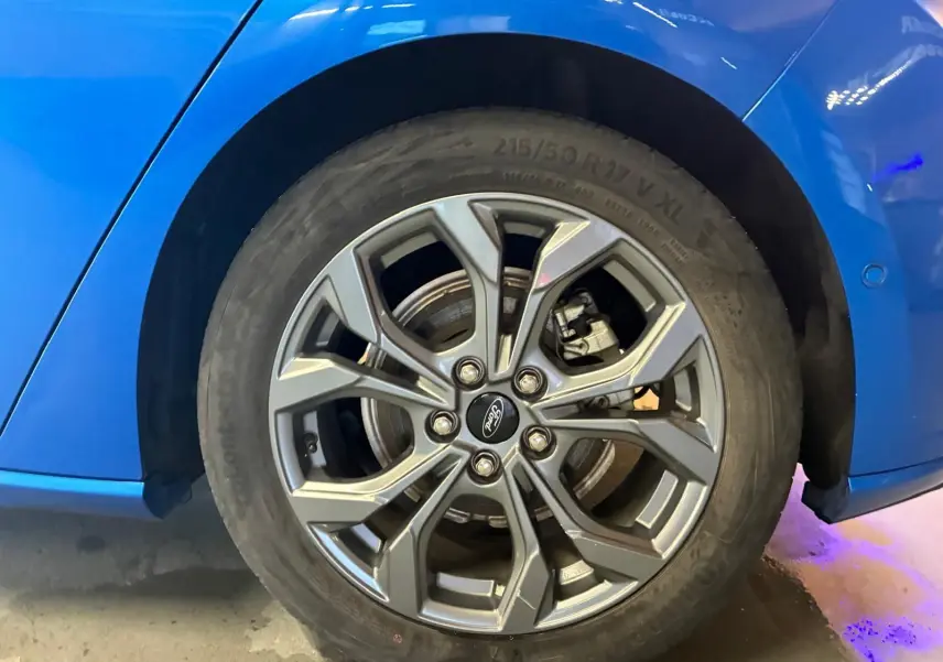 Gros plan sur la roue avant droite d’une Ford Focus bleu vif, mettant en valeur la jante alliage au design moderne.