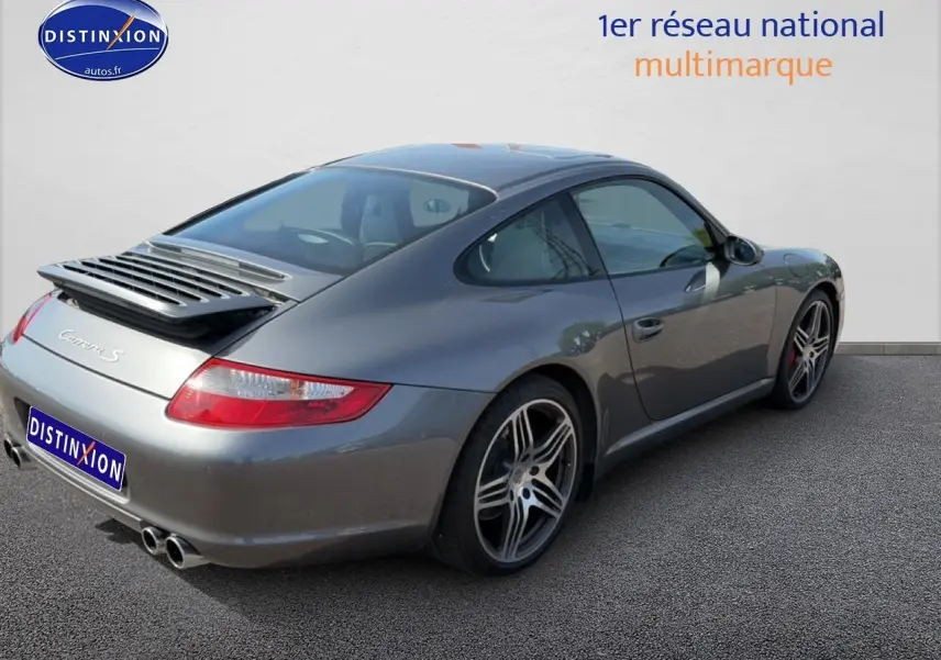Porsche 911 (997) Carrera S gris vue 3/4 arrière droit, jantes alu et aileron arrière déployé.