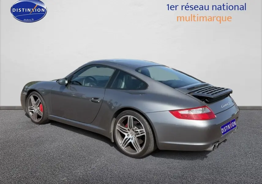 Porsche 911 (997) Carrera S gris vue 3/4 arrière droit, avec jantes alu et aileron arrière déployé.