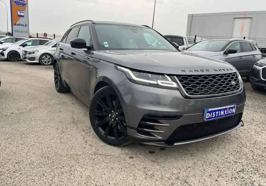 Range Rover Velar gris ammonite en 3/4 avant droit avec jantes noires 21 pouces et calandre hexagonale distinctive.