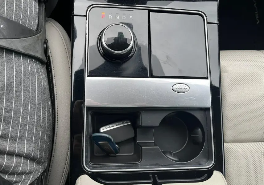 Vue plongeante sur la console centrale noire brillante du Range Rover Velar gris Ammonite avec clé Loisirs et porte-gobelet.