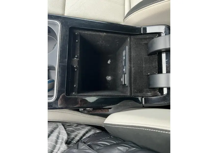 Vue rapprochée de la console centrale ouverte du Range Rover Velar, avec accoudoir en cuir beige et finition noire brillante.