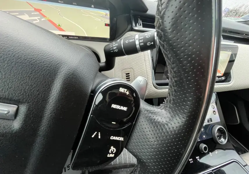Gros plan sur le volant en cuir perforé noir du Range Rover Velar 2017, avec commandes de régulateur et écran de navigation visible.
